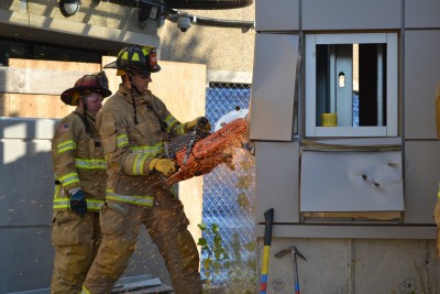 Lt. Wendell Cote supervises as a probationary firefighter saws into the metal skin of the exterior. The nearby window was removed intact. (Chris DeFrancesco/UConn Health)